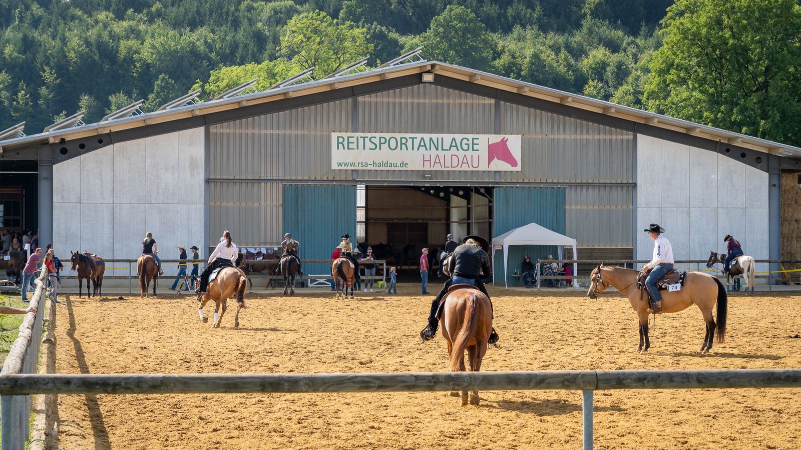 Reiter auf dem Außenreitplatz der Reitsportanlage Haldau, dahinter die Halle mit dem Schriftzug Reitsportanlage Haldau