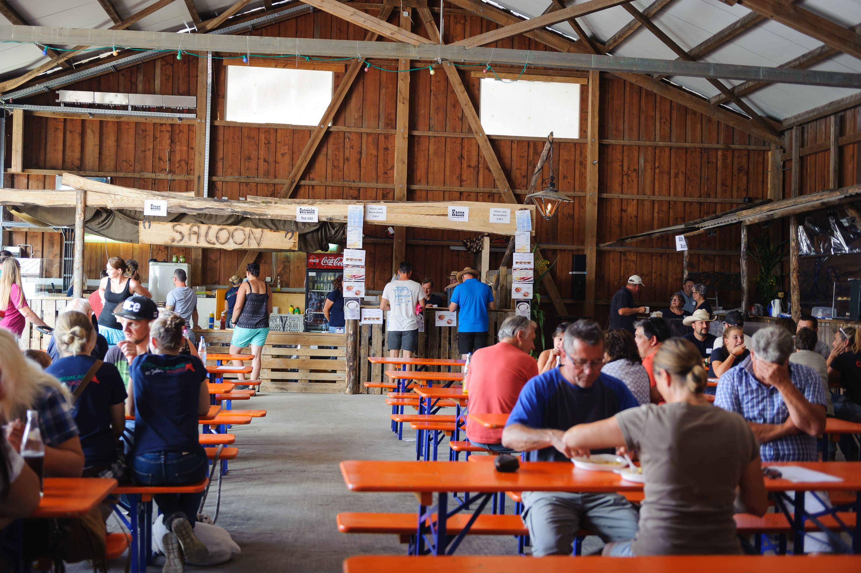 Gäste sitzen bei einer Veranstaltung an Biertischen in der Scheune, hinten die Theke