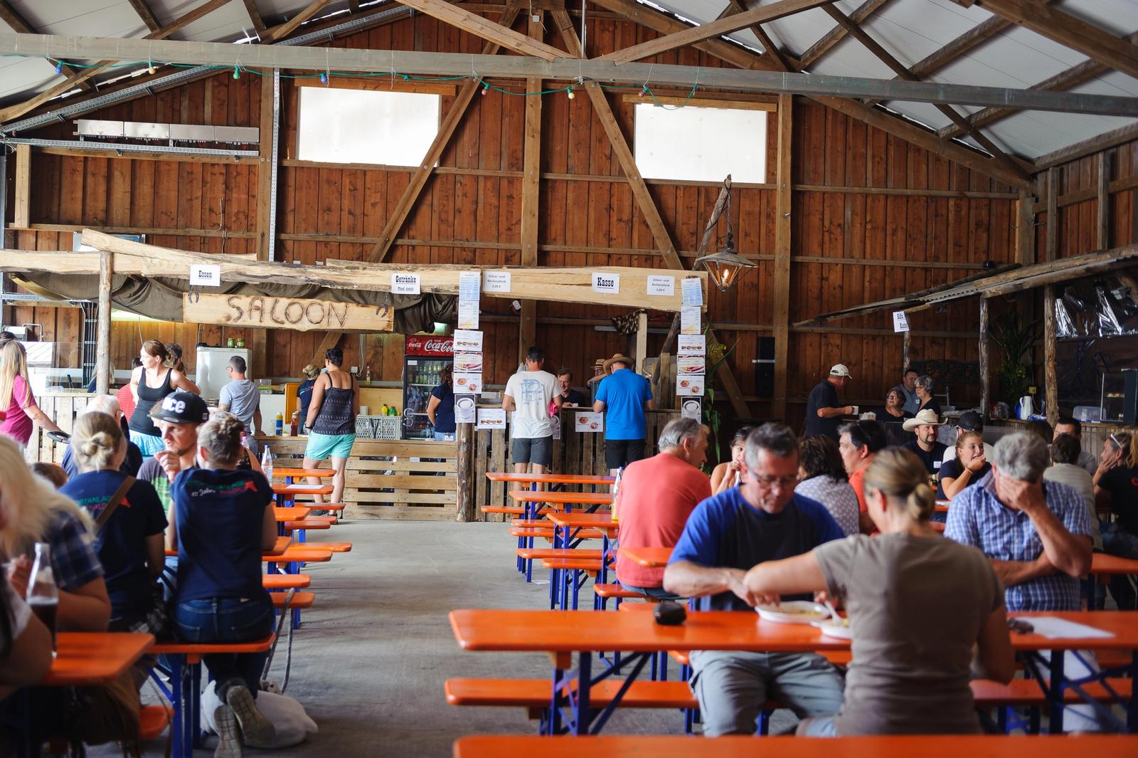 Gäste sitzen bei einer Veranstaltung an Biertischen in der Scheune, hinten die Theke