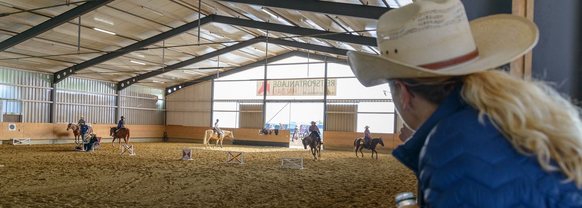 Westernreiter beim Turnier in der Reithalle der Reitsportanlage Haldau, im Vordergrund eine Zuschauerin mit Cowboyhut