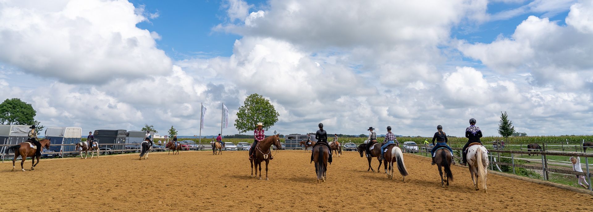 Reiter auf dem Außenreitplatz der Reitsportanlage Haldau, im Hintergrund Pferdeanhänger und Fahnen