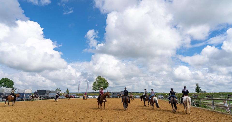 Reiter auf dem Außenreitplatz der Reitsportanlage Haldau, im Hintergrund Pferdeanhänger und Fahnen
