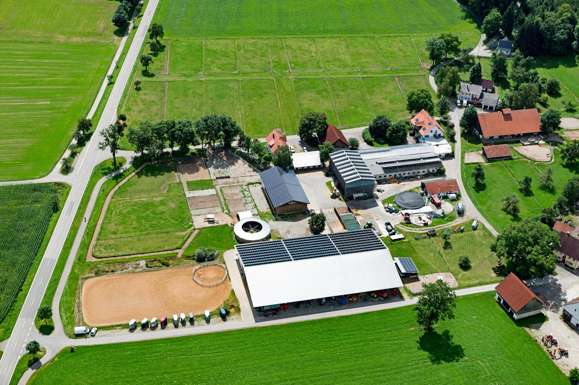 Luftbild der Reitsportanlage Haldau: Reithalle mit Photovoltaik-Dach, Außenplatz, Longierzirkel, Koppeln und Hof