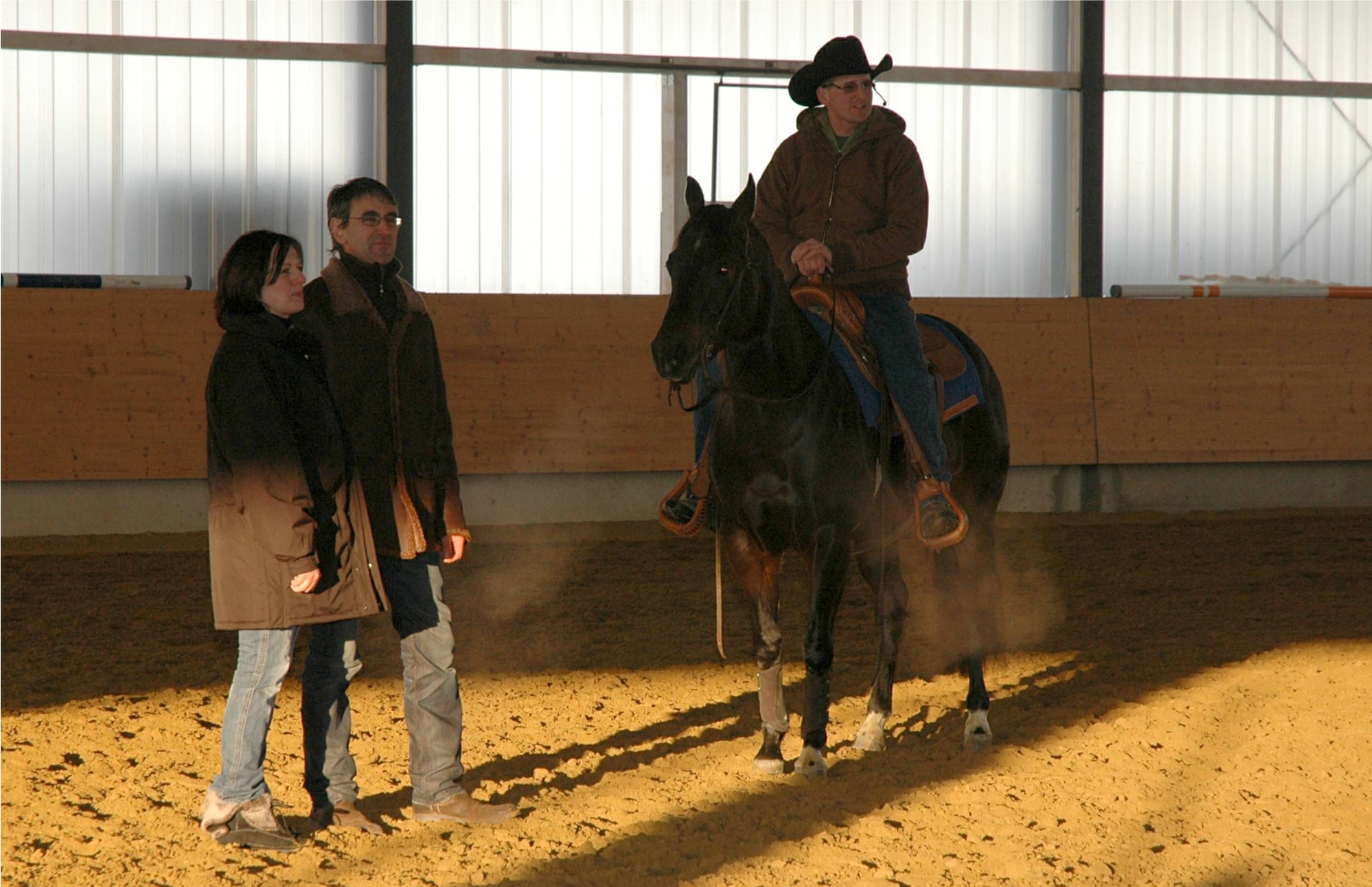 Westernreiter auf einem dunklen Pferd in der Reithalle der Reitsportanlage Haldau, daneben zwei zuschauende Personen