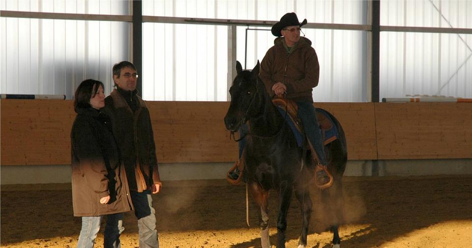 Westernreiter auf einem dunklen Pferd in der Reithalle der Reitsportanlage Haldau, daneben zwei zuschauende Personen