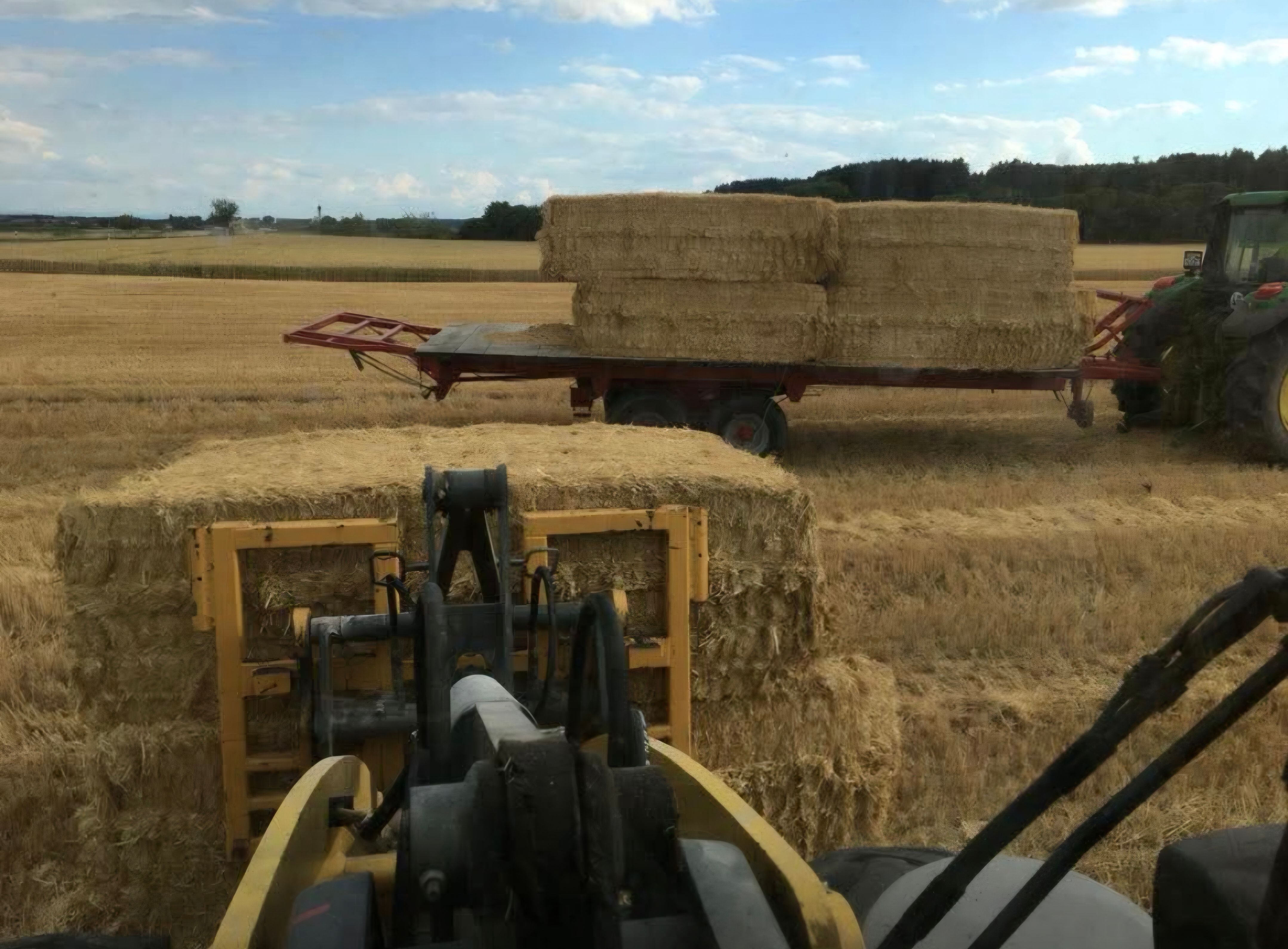 Frontlader lädt Strohballen auf einen Anhänger auf dem abgeernteten Feld