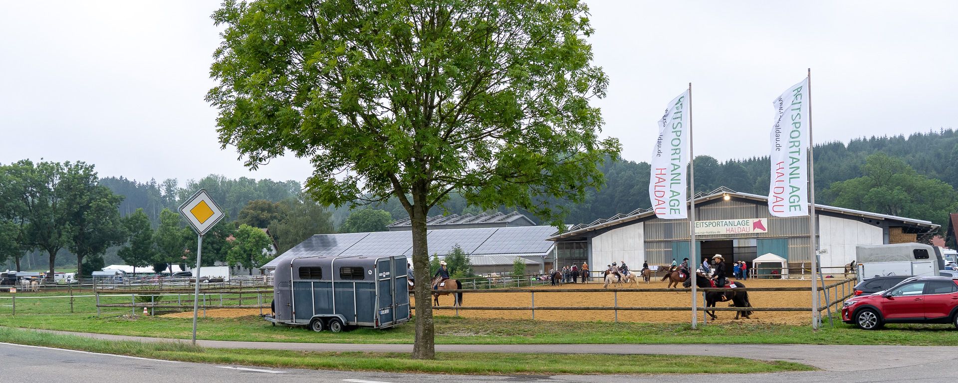 Die Reitsportanlage Haldau mit Werbefahnen und Reitplatz, Reiter vor der Halle