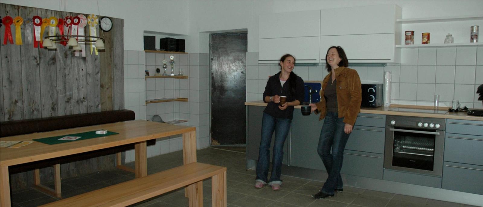 Reiterstübchen der Reitsportanlage Haldau mit Küchenzeile, Holztisch und Turnierschleifen an der Altholzwand