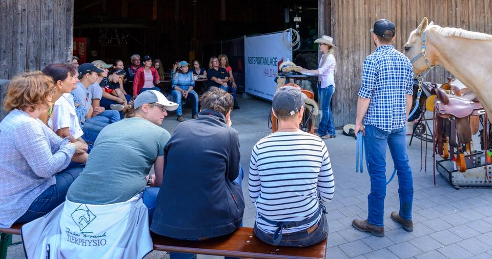 Trainer erklärt einer Gruppe Reiterinnen und Reiter vor der Scheune die Arbeit am Pferd